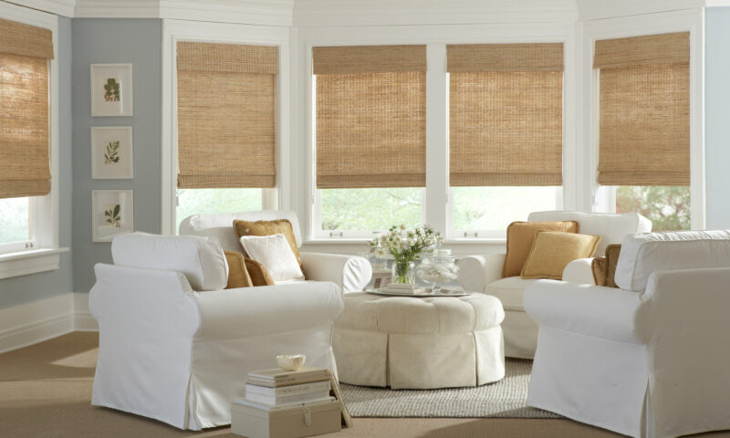 A bright sitting room features natural woven shades that bring warmth, texture, and an organic touch to the clean white furnishings and soft décor