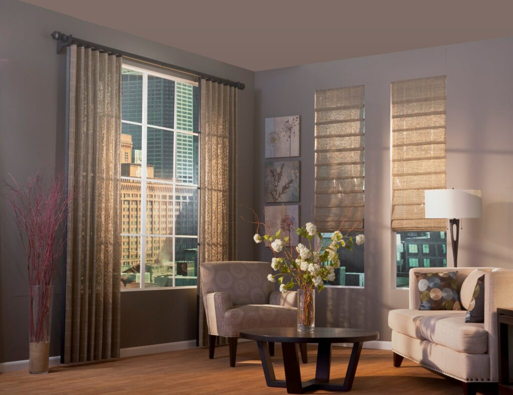 Contemporary living room with large windows featuring vertical blinds paired with Roman shades, complementing neutral-toned furniture and modern decor