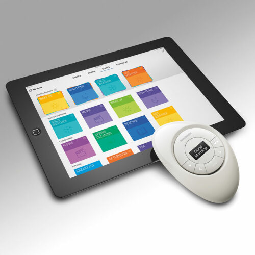 A tablet displaying a home automation app with colorful control options next to a remote control device for motorized window treatments