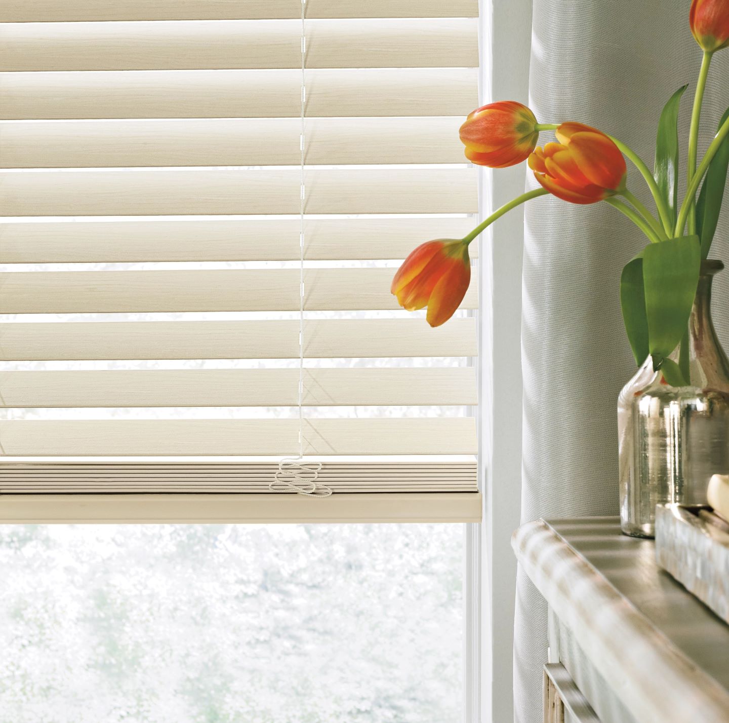 Close-up of beige window blinds next to an orange tulip arrangement in a vase.