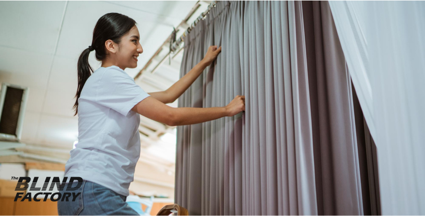 A woman adjusting a curtain, ensuring it hangs neatly and evenly, with a bright, cozy room in the background.