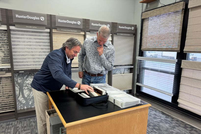 Customer selecting different types of window shades in a showroom with multiple shade styles displayed in the background.