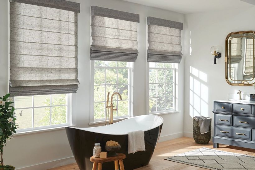 Bright, modern bathroom with a bathtub and mirror featuring elegant gray Roman shades on the window.