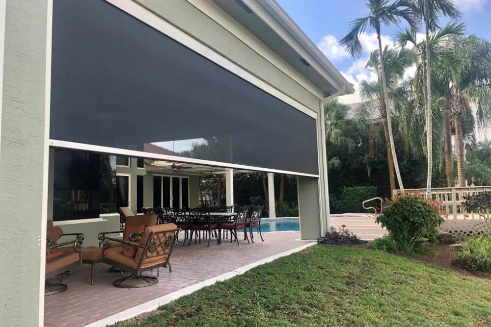 MagnaTrack exterior screen lowered over a covered patio with outdoor dining furniture